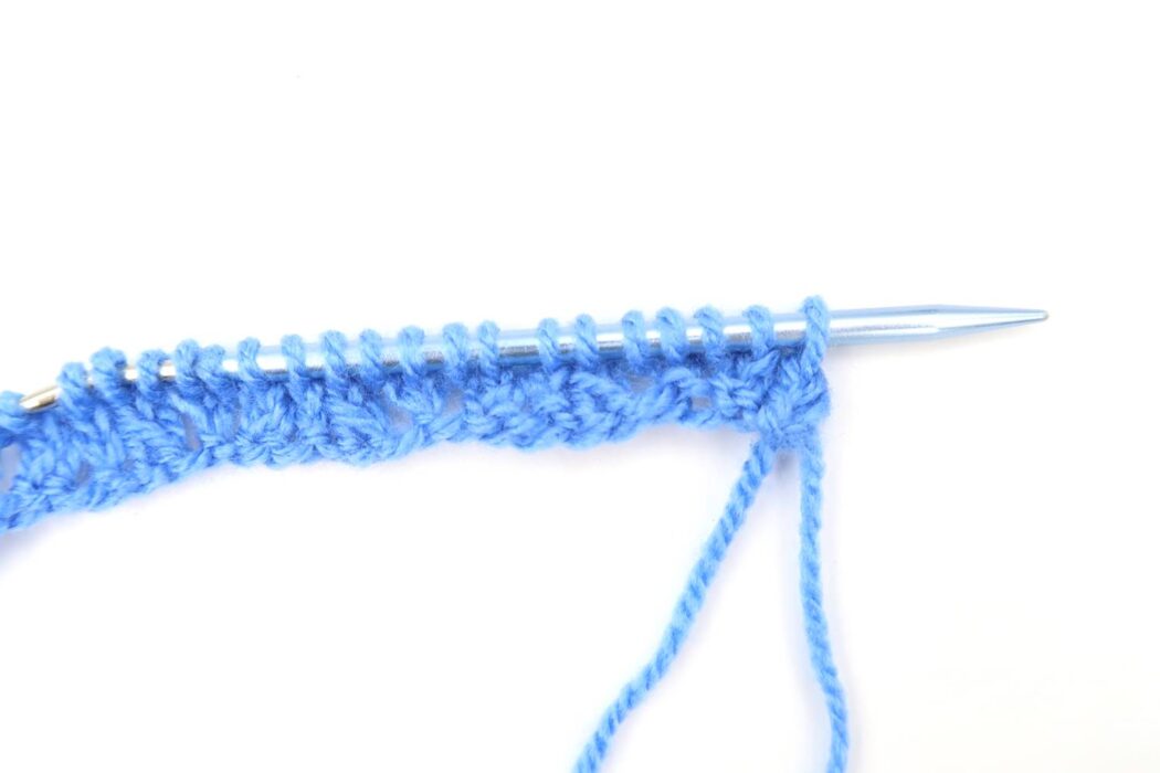 closeup of a knitting needle working on the ladder knit stitch pattern