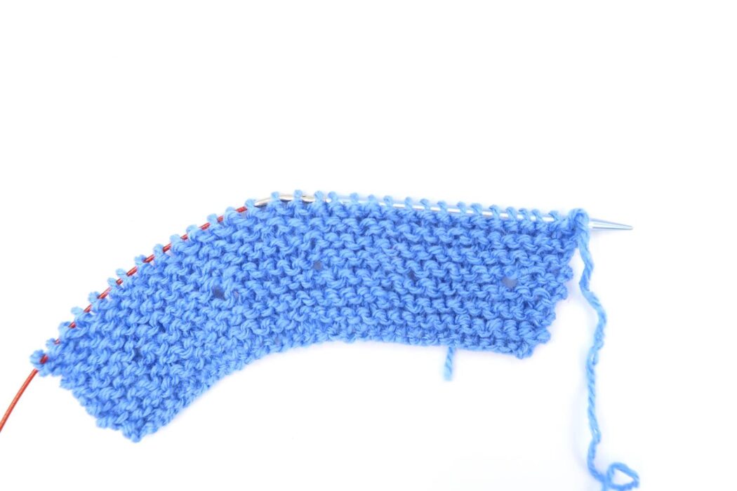 closeup of knitting needle working on strawberry seed stitch