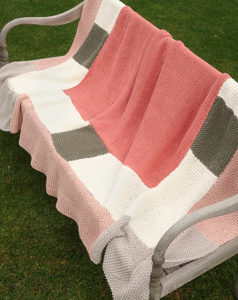 easy blanket knitting pattern on a bench viewed from an angle to show the entire blanket pattern