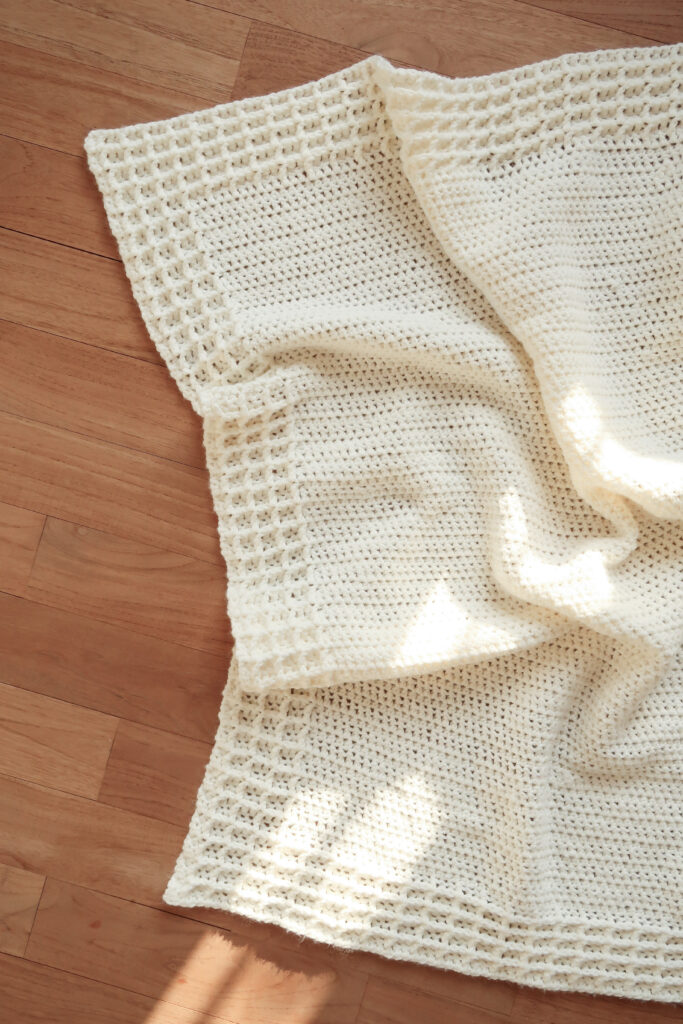 Esme waffle stitche crochet blanket pattern laid out on a wooden floor