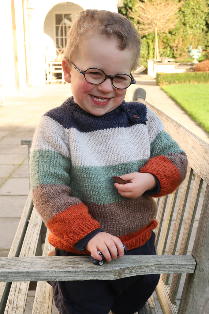 Little boy wearing the striped children knit sweater pattern on a bench