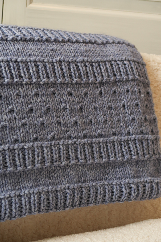 close-up of the free stitch pattern repeat for the blue chunky knit blanket pattern folded over a pale couch
