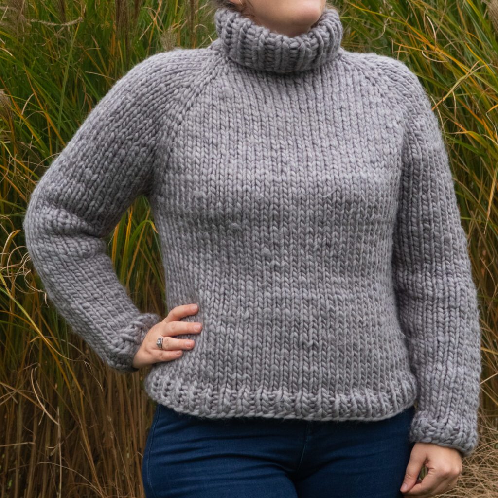 close-up of a woman wearing a gray raglan sweater knitting pattern in natural daylight