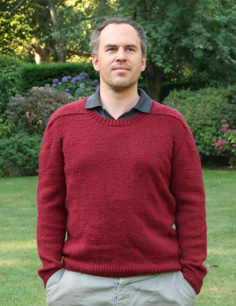 Man wearing the finished Out and About sweater made from this knitting pattern for mens sweater in dark red DK yarn
