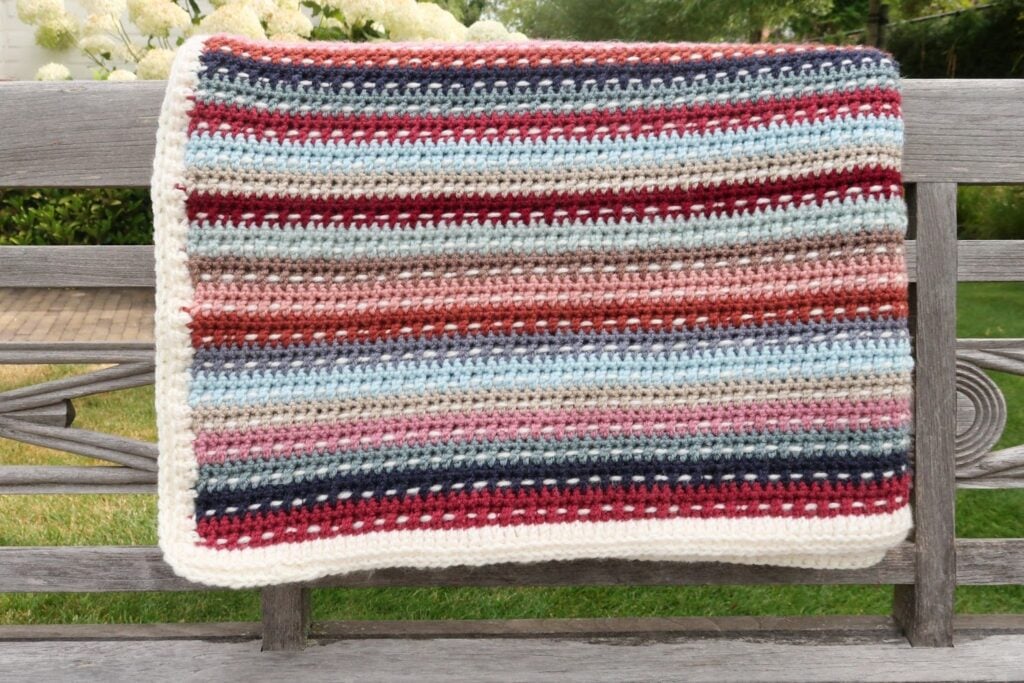 Colorful striped scrap yarn crochet blanket folded on a garden bench