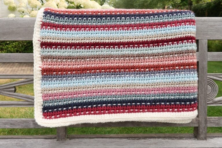 Colorful striped scrap yarn crochet blanket folded on a garden bench