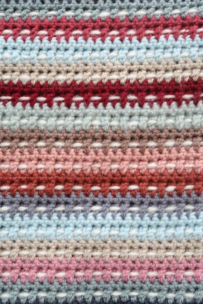 Close up of a scrappy crochet afghan showing scrap yarn woven between the double crochet rows
