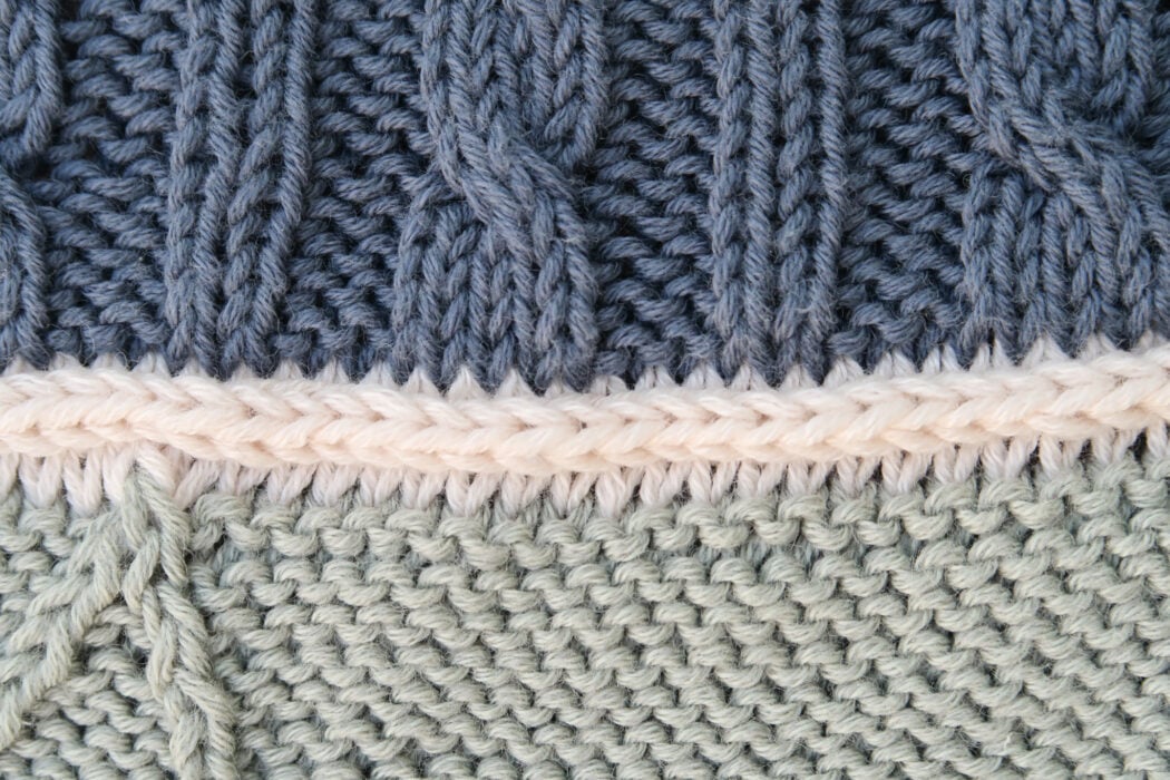 Close-up of the cream Goose Down divider row between two color sections on the Step into Cables Shawl Knitalong