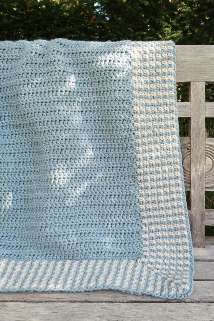 Finished moss stitch crochet blanket pattern laid flat, showing the blue center and cream border