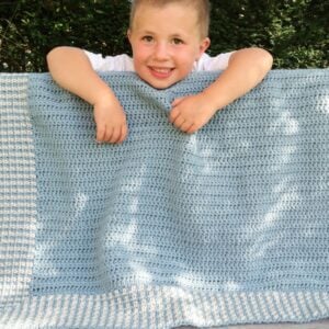 Moss stitch crochet baby blanket in blue and cream draped over a child's shoulders, from the moss stitch crochet blanket pattern